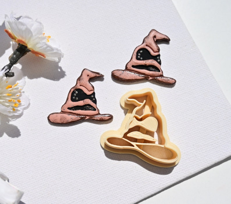 Op de afbeelding: Drie koekjesvormen in de vorm van de Sorteerhoed uit de Harry Potter-serie. De vormen zijn gemaakt van plastic en zijn in verschillende tinten bruin en zwart.