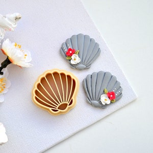 Könnte beinhalten: Zwei graue Fondant-Muscheln mit weißen und roten Blumenakzenten und einem Plastik-Muschel-Ausstecher.