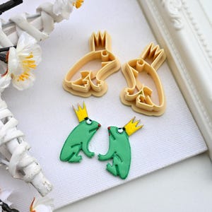 May include: Two green frog cookie cutters with yellow crowns and two matching frog cookies with yellow crowns.