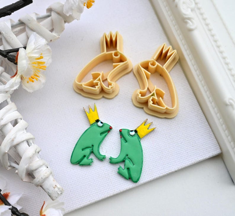 May include: Two green frog cookie cutters with yellow crowns and two matching frog cookies with yellow crowns.
