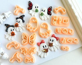 Op de afbeelding: Een verzameling Halloween-thema knutselbenodigdheden, waaronder spook- en vlindervormige mallen, samen met spookbeeldjes met pompoenen en boeken. De beeldjes hebben zwarte hoeden en rode strikken. De mallen zijn lichtoranje.