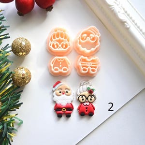 K&ouml;nnte beinhalten: Weihnachtliche Ausstecher und dekorative Ornamente. Die Ausstecher haben die Form von Weihnachtsmann und Frau Claus sowie deren Outfits. Die Ornamente sind goldfarben und die Figuren sind rot, wei&szlig; und schwarz.