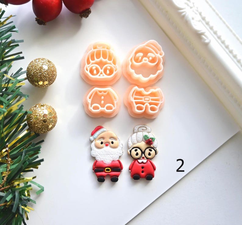 K&ouml;nnte beinhalten: Weihnachtliche Ausstecher und dekorative Ornamente. Die Ausstecher haben die Form von Weihnachtsmann und Frau Claus sowie deren Outfits. Die Ornamente sind goldfarben und die Figuren sind rot, wei&szlig; und schwarz.