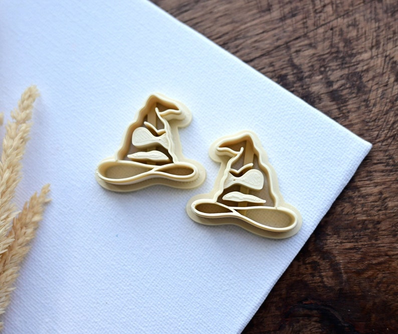 Op de afbeelding: Twee beige plastic koekjesvormen in de vorm van de Sorteerhoed uit de Harry Potter-serie.