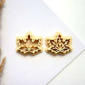 Könnte beinhalten: Zwei Plastik-Ausstecher in Form von Ahornblättern. Die Ausstecher sind beige und haben ein detailliertes Design.