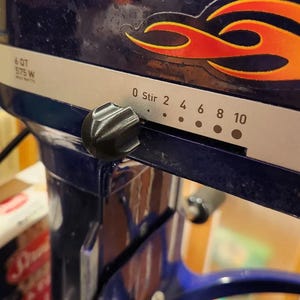 May include: A blue stand mixer with a silver control panel and a black knob. The control panel has a speed dial with numbers 0 through 10 and the words "Stir" and "0".