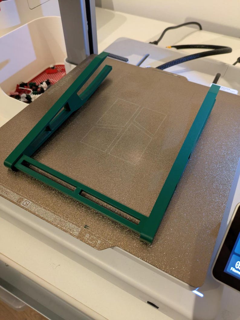 May include: A green plastic frame sits on a textured, light brown surface. The frame has a rectangular shape with a grid pattern inside.