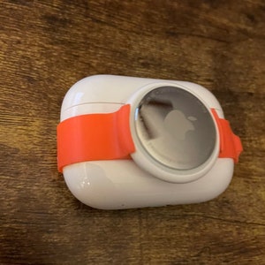 May include: White wireless charging case with an orange silicone strap. The case has a silver Apple logo on the front.