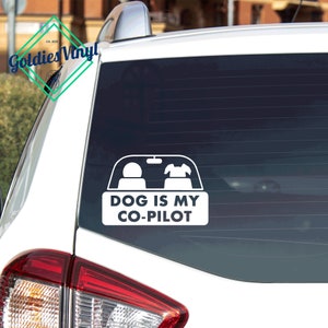 May include: White vinyl car sticker with a silhouette of a person and a dog in the driver's seat of a car. The text reads "DOG IS MY CO-PILOT".