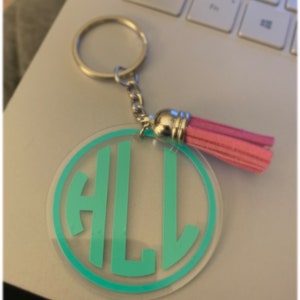 May include: A teal blue acrylic keychain with the letters "ALL" in a circle. The keychain has a silver chain and a pink tassel.