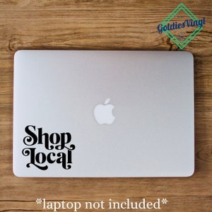 Peut inclure: Un autocollant noir et blanc avec le texte "Shop Local" dans une police rétro sur un ordinateur portable argenté.