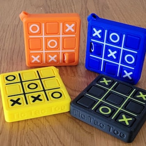 May include: Four different colored Tic Tac Toe games. The games are yellow, orange, blue, and black. Each game has the words "Tic Tac Toe" printed on the bottom.