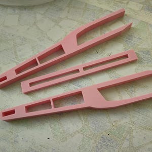May include: Three pink plastic tweezers with different designs. The tweezers are used for crafts, hobbies, and other tasks.