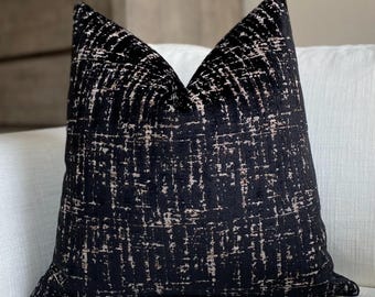May include: A square decorative pillow with a black background and a textured pattern in off-white. The pillow is placed on a white sofa. The pillow has a soft, velvety appearance, adding a touch of elegance to any living space.