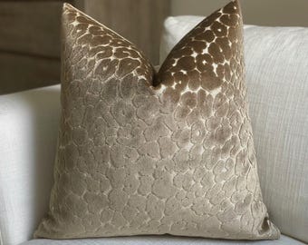May include: A decorative throw pillow with a tan and brown spotted pattern. The pillow has a soft, textured surface and is placed on a white sofa. The pillow's design resembles a leopard print.