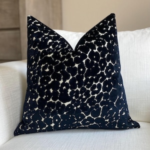 May include: A decorative throw pillow with a black and white spotted pattern. The pillow has a dark navy blue background with a repeating pattern of white spots. The pillow is square and has a soft, textured appearance.