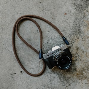 May include: A silver camera with a brown leather strap. The camera has a black lens with the text "Canon Lens FD 1:1.2 55mm 1:16" printed on it. The camera also has the text "FUJIFILM X-T10" printed on it.