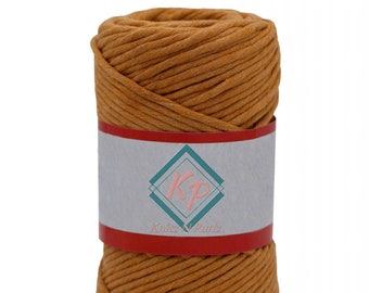 May include: A spool of golden-brown yarn, tightly wound and ready for crafting. A white label with a teal and pink logo and the text "Knitz N Purlz" wraps around the center. The yarn is a warm, earthy tone, perfect for various knitting or crochet projects.
