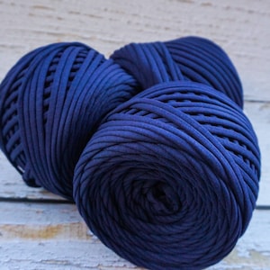May include: Three balls of dark blue yarn, made from recycled t-shirts, are stacked on a white wooden surface.