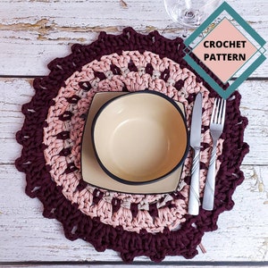Könnte beinhalten: Handgefertigter gehäkelter Platzdeckchen in Burgunder- und Rosatönen mit gewelltem Rand. Eine beige Schüssel und ein quadratischer Teller sind auf dem Platzdeckchen platziert, zusammen mit Besteck. Der Text "CROCHET PATTERN" befindet sich oben rechts.