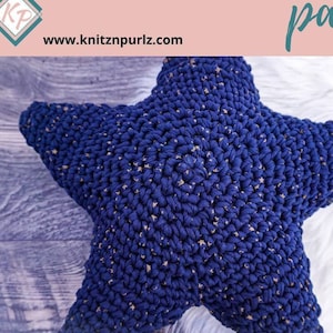 Op de afbeelding: Een blauwe, gehaakte stervormige kussenhoes met gouden spikkels. De kussenhoes ligt op een wit, pluche oppervlak. De tekst "STAR CROCHET PILLOW CASE pattern" staat op een roze achtergrond. Het websiteadres "www.knitznpurls.com" staat onder de tekst.
