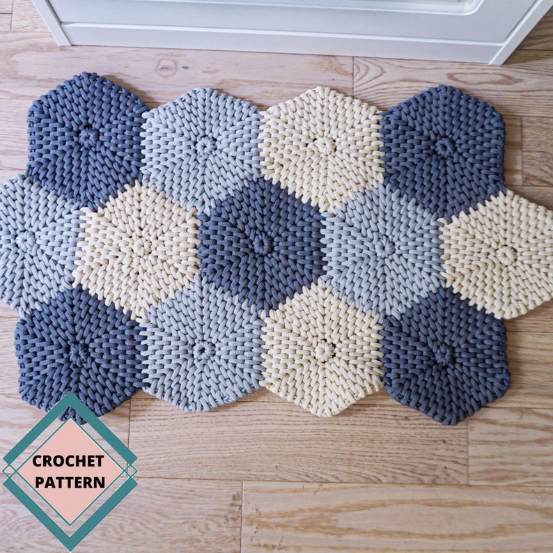 Puede incluir: Una alfombra tejida a crochet hecha de hilo beige, azul claro y azul oscuro. La alfombra est&aacute; hecha de formas hexagonales y tiene una etiqueta "CROCHET PATTERN" en la esquina inferior izquierda.