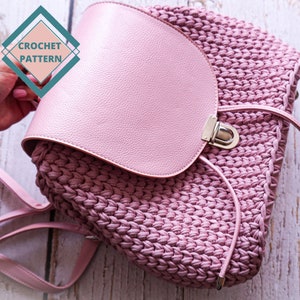 May include: A pink crocheted backpack with a leather flap and a silver buckle. The backpack has a long strap.