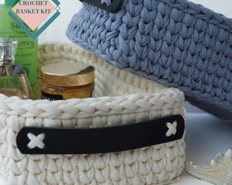 Puede incluir: Dos cestas de crochet, una blanca y otra azul, con asas de cuero negro. Las cestas están llenas de varios artículos, incluyendo una botella de loción, un tarro de crema y un pequeño frasco de perfume. El texto "CROCHET BASKET KIT" es visible en la esquina superior izquierda de la imagen.