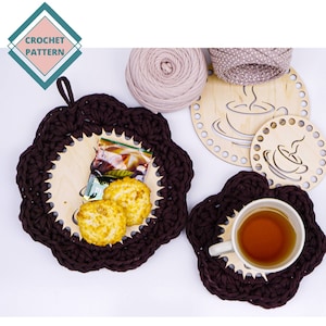 Op de afbeelding: Twee bruine gehaakte onderzetters met houten inleg. De grotere onderzetter heeft een houten inleg met een theezakje en twee crackers. De kleinere onderzetter heeft een houten inleg met een kopje thee.