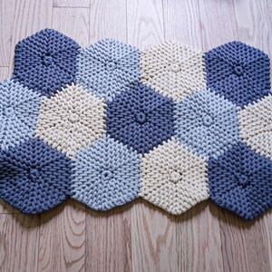 Puede incluir: Una alfombra tejida con cuerda gruesa en tonos azules y crema. La alfombra tiene forma de panal de abejas con secciones hexagonales.
