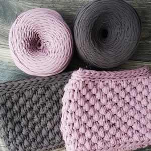 May include: Two balls of yarn, one pink and one dark gray, and two crocheted squares, one pink and one dark gray.