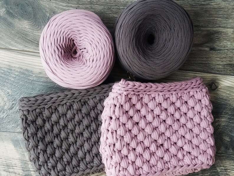 May include: Two balls of yarn, one pink and one dark gray, and two crocheted squares, one pink and one dark gray.