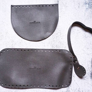 May include: Three pieces of gray leather for a DIY bag project. The pieces include a rectangular base, a curved top flap, and a long strap with two adjustable buckles. The leather is embossed with the text "OG MARMELATTA".