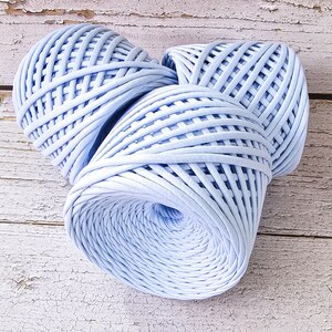May include: Three skeins of light blue yarn, each wound into a round shape with a criss-cross pattern. The yarn is made of a soft, textured material.