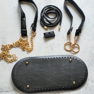 May include: A black leather bag with gold chain straps and a black leather base with a decorative stitch pattern. The bag has two black leather straps with gold hardware.