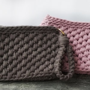May include: Two crocheted bags, one in a dark brown color and one in a light pink color. The brown bag has a handle and a gold ring.