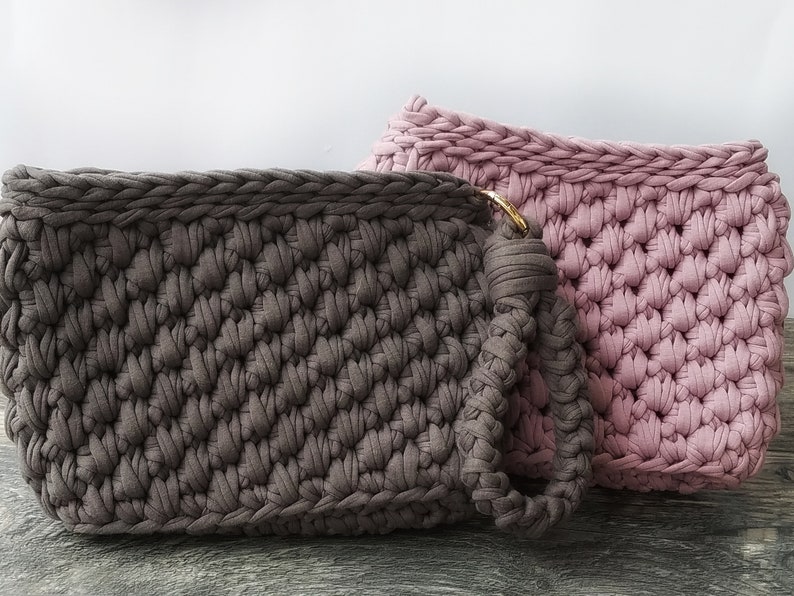 May include: Two crocheted bags, one in a dark brown color and one in a light pink color. The brown bag has a handle and a gold ring.