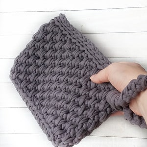 May include: A gray crocheted clutch bag with a long strap. The bag is made from thick yarn and has a textured surface.