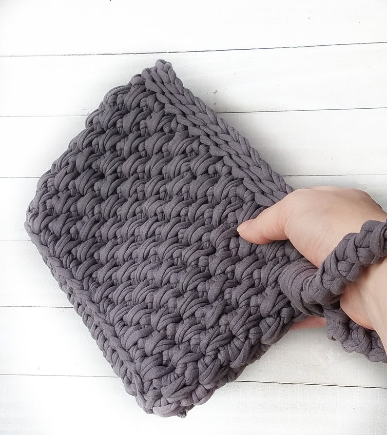 May include: A gray crocheted clutch bag with a long strap. The bag is made from thick yarn and has a textured surface.