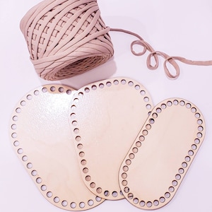 May include: Three wooden oval-shaped loom bases with holes around the edges. The bases are different sizes and are arranged in a triangular shape. A ball of beige yarn is in the background.