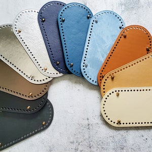 May include: Nine different colored leather handbag base shapes with a variety of stitching patterns. The bases are all oval shaped and have a hole pattern around the edges.