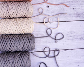 May include: Five spools of yarn in various shades of brown, beige, and gray. Each spool is wrapped with a different color of yarn, and the yarn is arranged in a vertical line. The yarn is tied together with a matching color of string.
