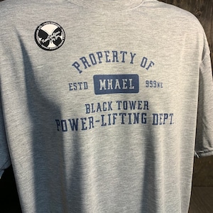 May include: Grey heather t-shirt with a navy blue print that reads "PROPERTY OF ESTO MHAEL 999NE BLACK TOWER POWER-LIFTING DEPT".