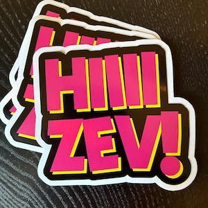 Könnte beinhalten: Ein Stapel Aufkleber mit dem Text "HIIII ZEV!" in leuchtendem Pink, gelb umrandet, auf schwarzem Hintergrund. Die Aufkleber haben einen weißen Rand und eine abgerundete rechteckige Form.