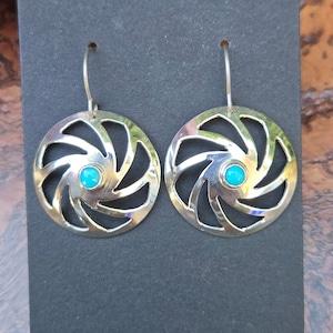 May include: Silver earrings with a turquoise stone in the center of each earring. The earrings are in the shape of a spiral with a cutout design.