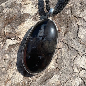 May include: A black and white oval pendant with a silver setting, hanging from a black cord.