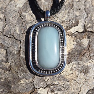 May include: A silver pendant necklace with a light blue oval stone set in a silver frame. The necklace is on a black cord.