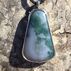 May include: A silver pendant with a green and white agate stone. The stone has a unique pattern of swirls and veins.