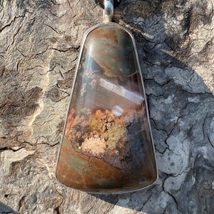 May include: A silver pendant with a large, irregularly shaped, brown, gray, and white agate stone. The stone has a unique, swirling pattern.