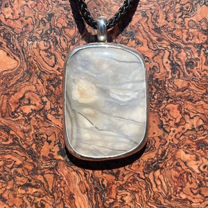 May include: A silver pendant with a white and gray agate stone. The pendant is on a black cord.